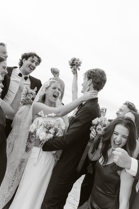 A bride laughing as her wedding party cheers around her